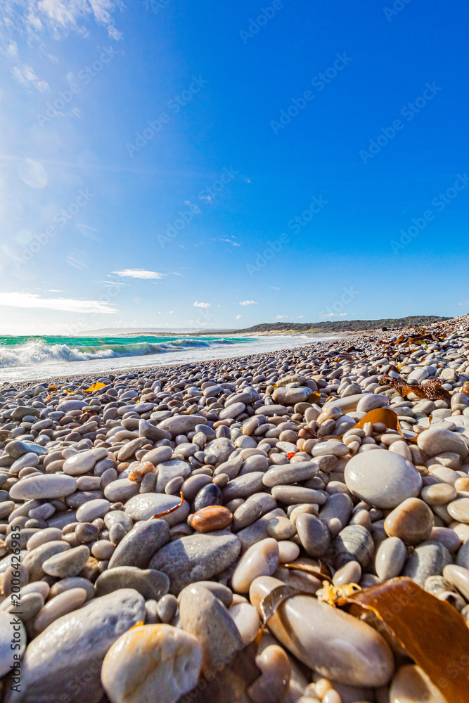 Obraz premium Tranquil coastline landscape with azure sky, sand, rocks, and gentle waves