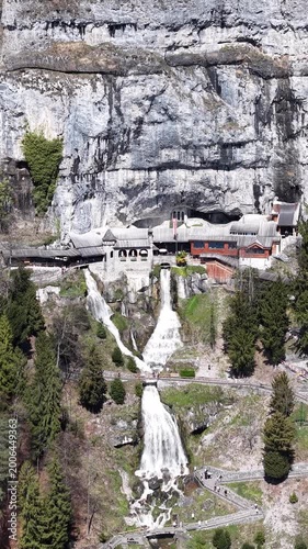 Aerial View of Saint Beatus Caves Entrance with Waterfall and Historic Buildings, Lake Thun, Switzerland