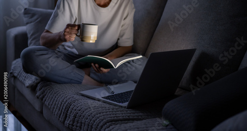 Photos Young woman working late on a sofa with laptop, notebook and coffee, focused in