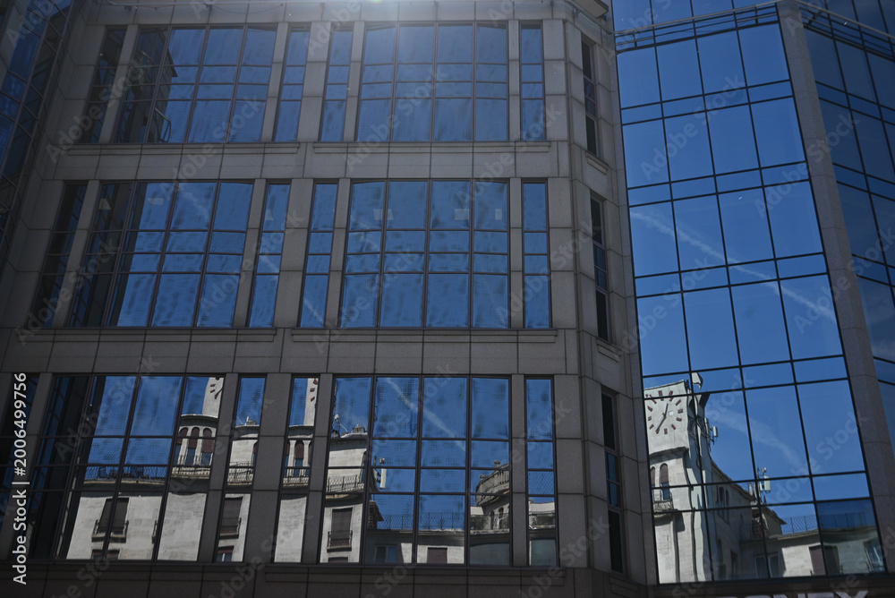 Obraz premium Reflection of historic architecture in a modern glass building facade on a clear day.