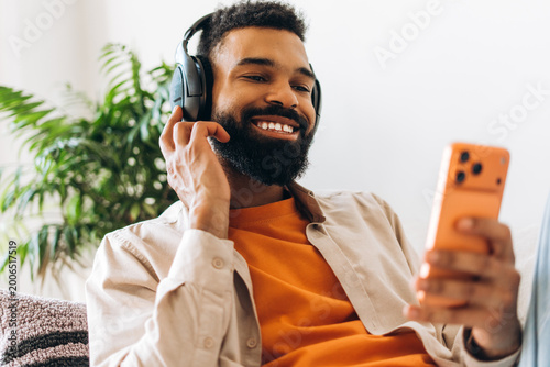 Canvastavla Happy black man enjoying music with headphones and smartphone