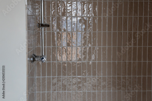 Photos Mur de douche moderne orné de petits carreaux rectangulaires beiges à la surface brillante, complété par une robinetterie métallique élégante dans un style épuré