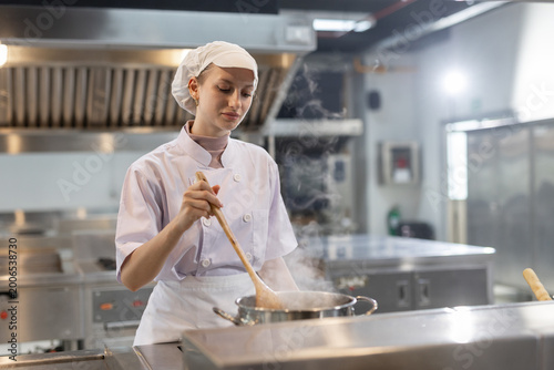 Foto female chef cooking food in a professional restaurant kitchen, stirring ingredients in a pan while preparing fresh cuisine with culinary skill, hygiene, and commercial food service concept