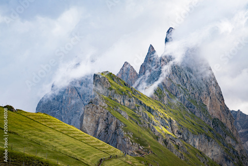 Seceda, Dolomites, Italy—lush green alpine ridge in South Tyrol with rising mist clouds from below. Dramatic overcast mountain landscape in the Alps, scenic hiking and travel destination.