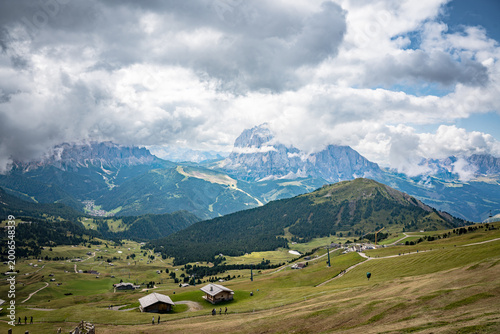 Ortisei, Val Gardena, Italy—alpine village in South Tyrol with distant Dolomite peaks rising above lush green valleys. Scenic Alps landscape with clear mountain views and travel appeal.