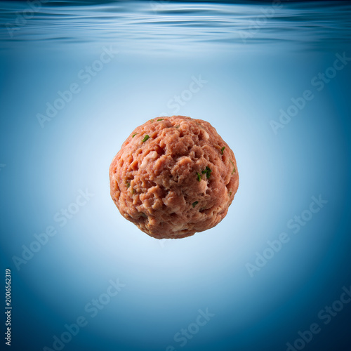 A single meatball floating in clear blue water isolated and centered.