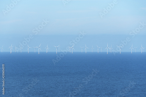 Schilderij op canvas Offshore wind turbines rise above the sea beneath a hazy blue horizon