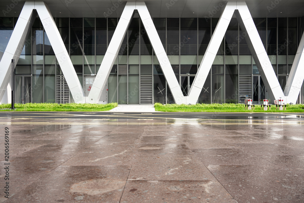 Fototapeta premium Modern architectural facade with V-shaped columns and wet plaza ground after rain