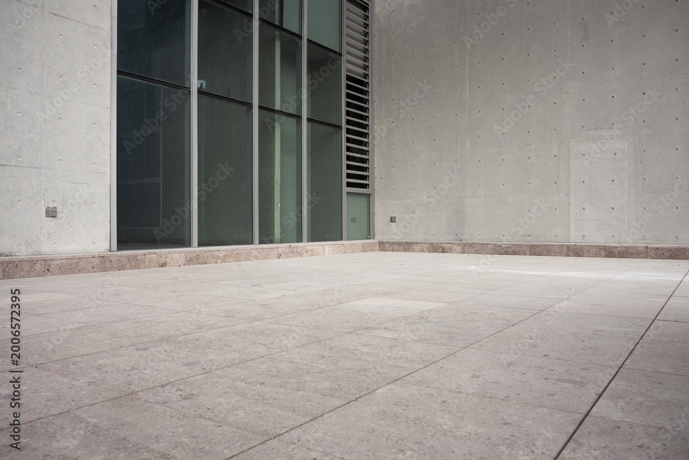 Fototapeta premium Modern architectural concrete wall with glass curtain wall and empty paved ground space