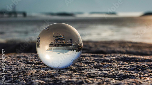 Fotografie A Crystal ball, Earth, Globe, world, glass ball placed on a rock beach, reflecting an inverted seascape and horizon with sunlight in the morning