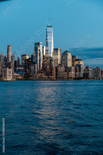 Lower Manhattan financial district skyline and One World Trade Center. Illuminated skyscrapers of Lower Manhattan reflecting in Hudson River during blue hour at sunset.