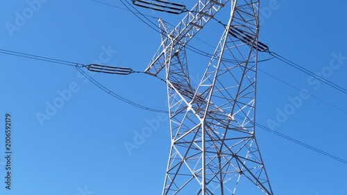 High voltage power line pylon against clear blue sky, low angle view of electrical grid infrastructure for renewable energy distribution and smart city power management systems.