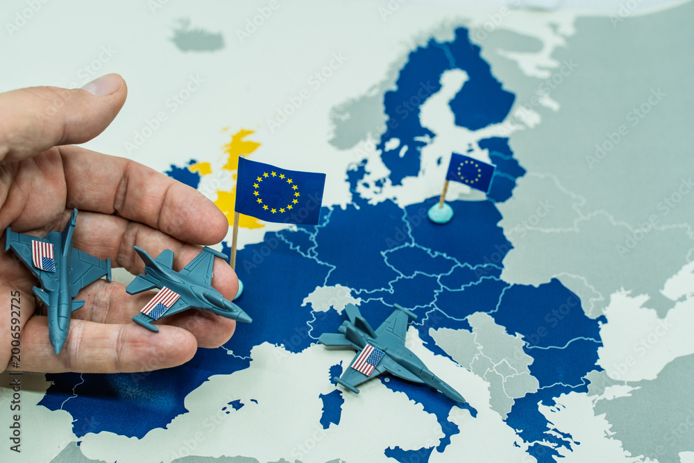 Fototapeta premium Hand withdrawing miniature toy fighter jets, representing United States troops, from a European map with European Union flags, symbolizing military withdrawal and changing geopolitics