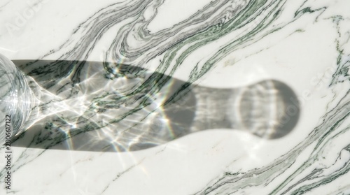 Glass of water casting a sharp shadow on a white marble surface with green veins, clean refracted light patterns