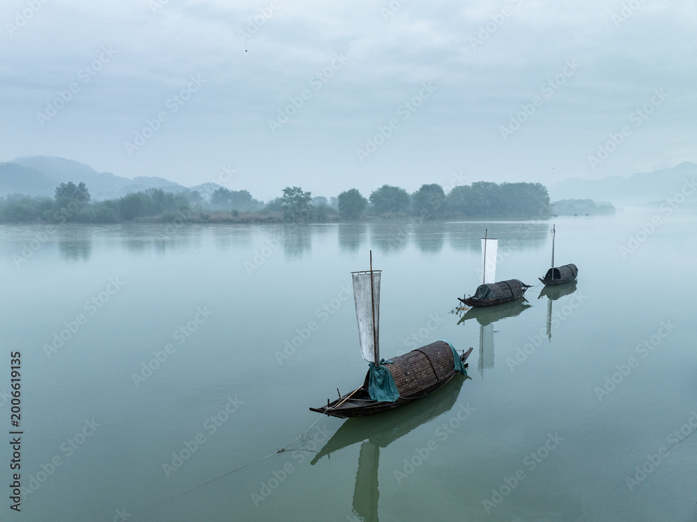 Obraz premium Three wooden boats quietly moored on a misty river with distant mountains in the background