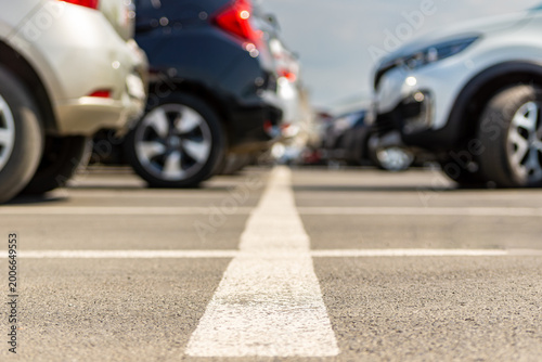 Low angle view of parking lot with white arrow marking on asphalt between parked cars