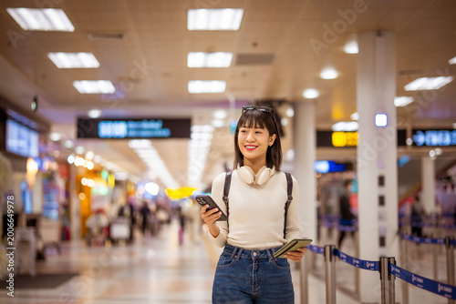 Traveler waiting in airport terminal with baggage and smartphone, checking flight schedule and departure information, capturing modern travel, navigation, and global journey experience.
