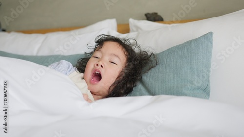 Konstfotografi A sleepy young child yawns widely while waking up in a comfortable white bed, a candid moment of childhood fatigue representing rest and domestic wellbeing