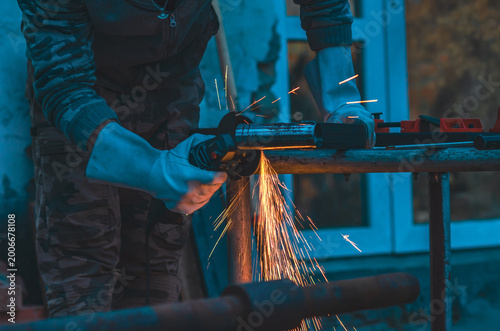 Worker grinding metal part using power tool. Visible sparks. Protective gloves, safety. Industry.