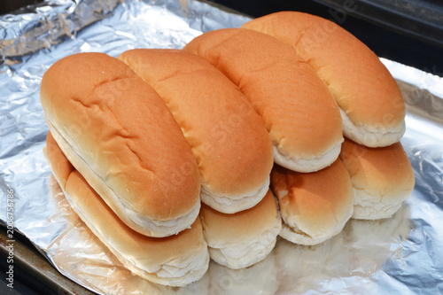 Quadro su tela Hotdog buns warming on a grill on foil, closeup.