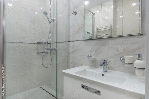 The bathroom features a shower with glass doors, a white sink with faucets, and mirrors on the walls. Natural light brightens the area, creating a clean look
