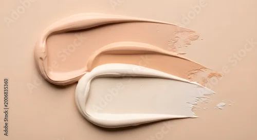 Obraz Three cosmetic foundation swatches spread on beige background showing different nude shades and textures of liquid makeup cream for skin tone matching beauty product testing.
