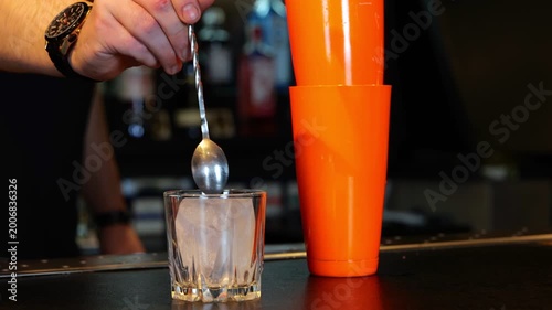 Male bartender working in a bar while making cocktail. Bartender putting a piece of ice into a glass. Cropped. Real time.