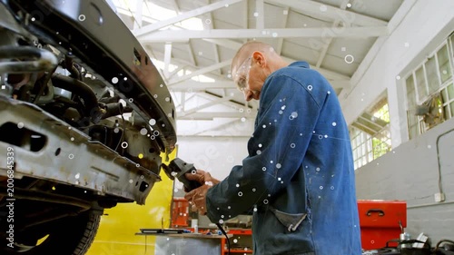 Mechanic starting grinder and grinding bumper for repair in automotive workshop, producing sparks