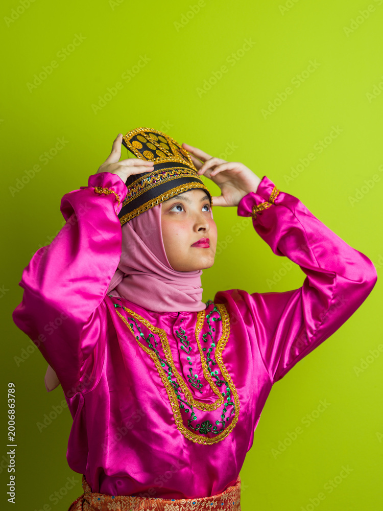 Obraz premium Young Woman Wearing Traditional Pink Southeast Asian Costume And Hijab Adjusting Embroidered Headdress