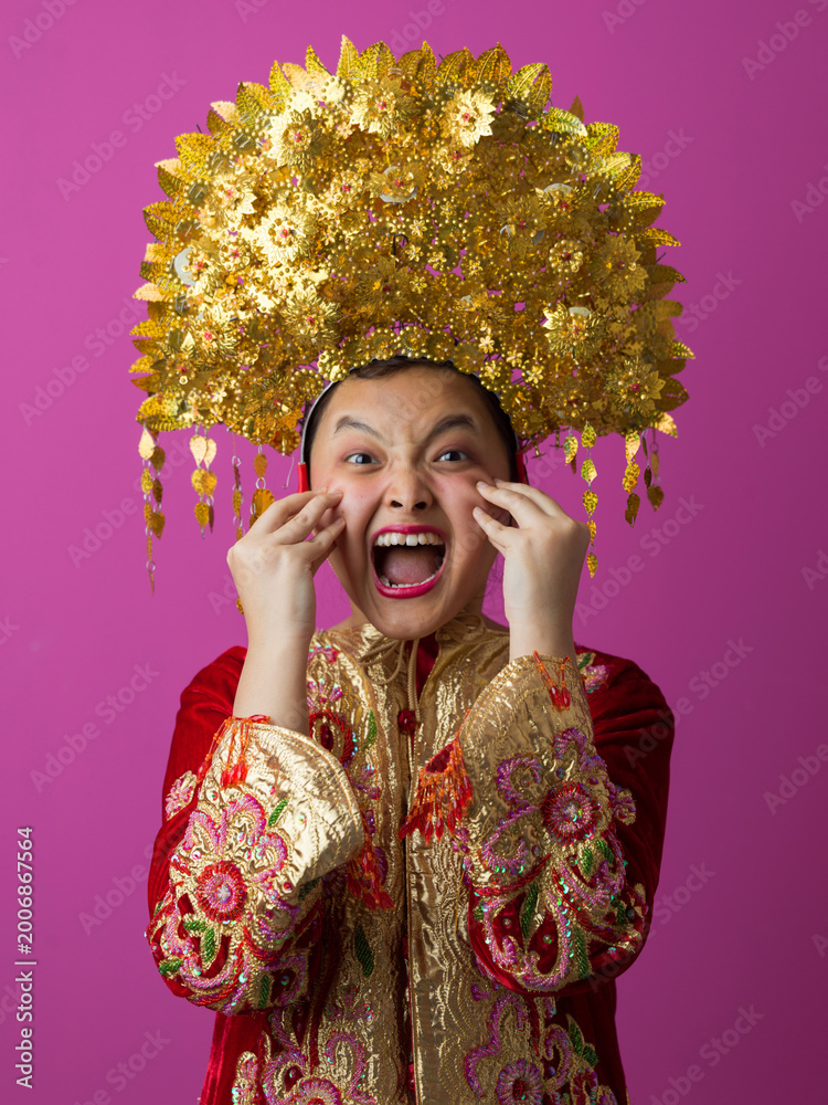 Fototapeta premium Excited Indonesian Asian Girl Wearing Traditional Gold Headdress and Embroidered Red Costume Celebrating Festival