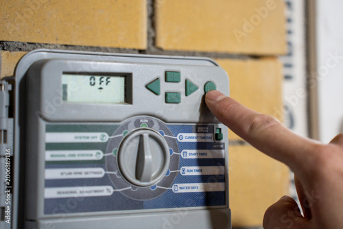 Foto Finger pressing button on irrigation controller panel, adjusting automatic watering system settings with digital display and selector dial