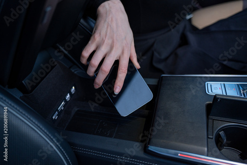 Foto Hand placing smartphone into open center console storage compartment inside modern car interior, with charging ports and cup holder visible