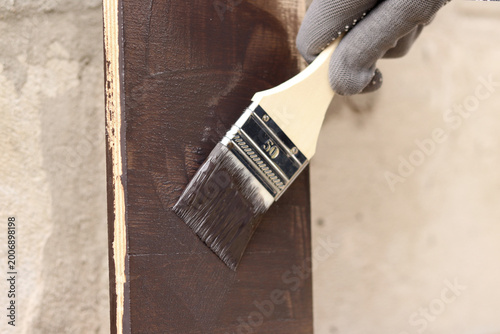 Painter covers a wooden panel with brown varnish, close-up. Hand in a protective glove holds a brush, painting a wooden surface. Handmade. The process of treating wood with a protective coating