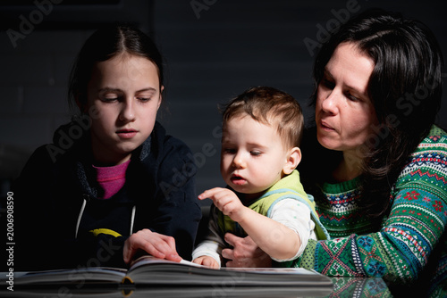Mother helping children read book, family learning together, natural candid home moment