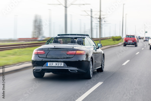 Black convertible driving on a highway in traffic. Rear view of a car in motion.