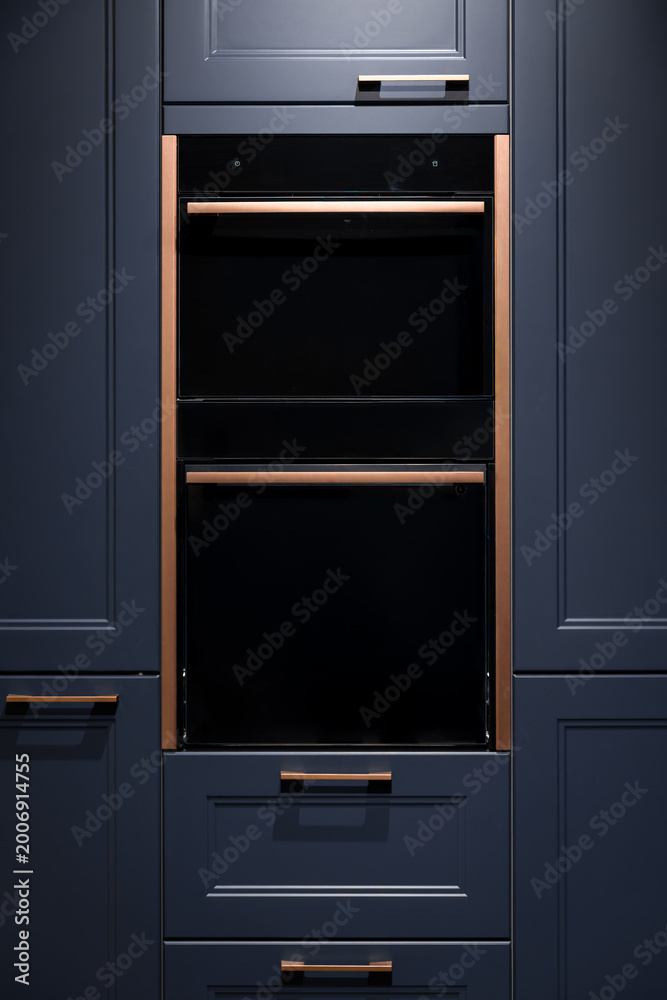 Fototapeta premium Built-in oven in dark blue cabinets. Elegant kitchen furniture with copper handles.