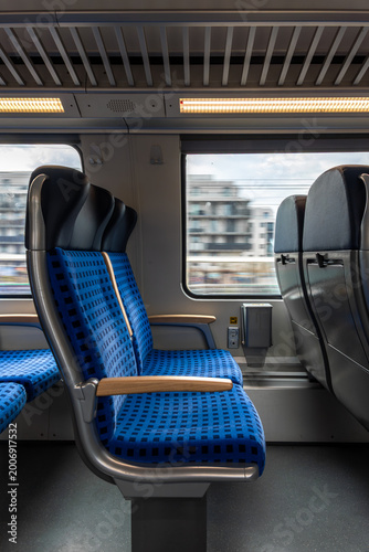 Interior of a passenger train with blue seats and large windows. The view outside is blurred.