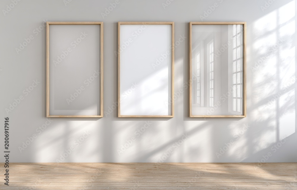 Fototapeta premium Three blank picture frames hanging on a white wall with natural light casting shadows.