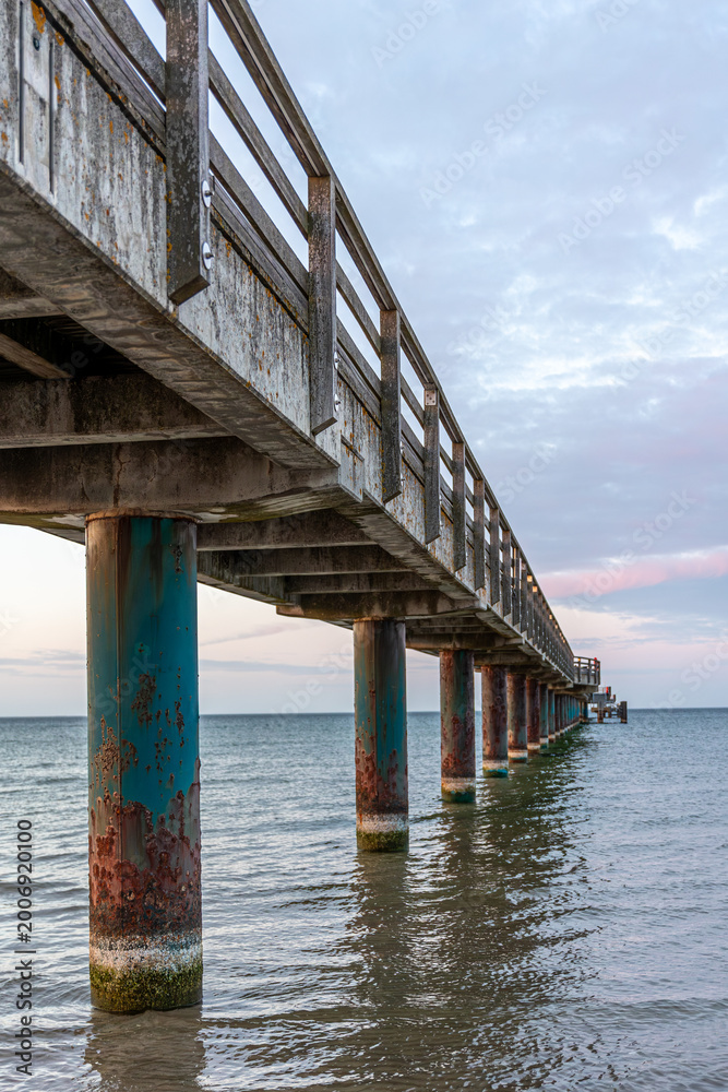 Fototapeta premium Vertical perspective under a sea bridge. Old columns in water during sunset.