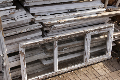 Old wooden window frames stacked in a pile. Frames are weathered and show signs of peeling paint.