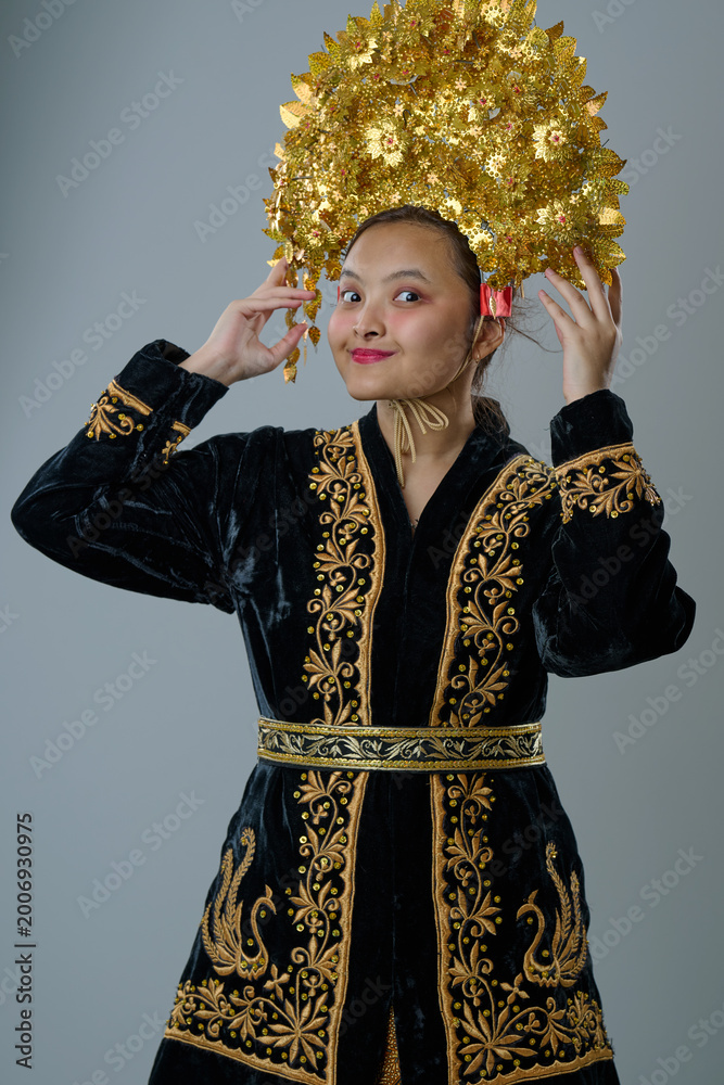 Fototapeta premium Young Indonesian Asian Woman Wearing Traditional Embroidered Black Robe and Ornate Gold Headdress Cultural Portrait