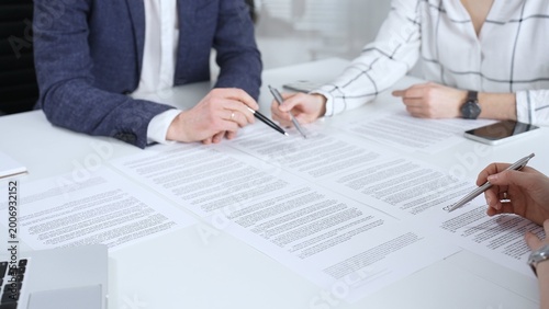 Professionals reviewing and signing contract documents across a white table, hands exchanging papers and pens to finalize negotiation, partnership and corporate agreement decisions