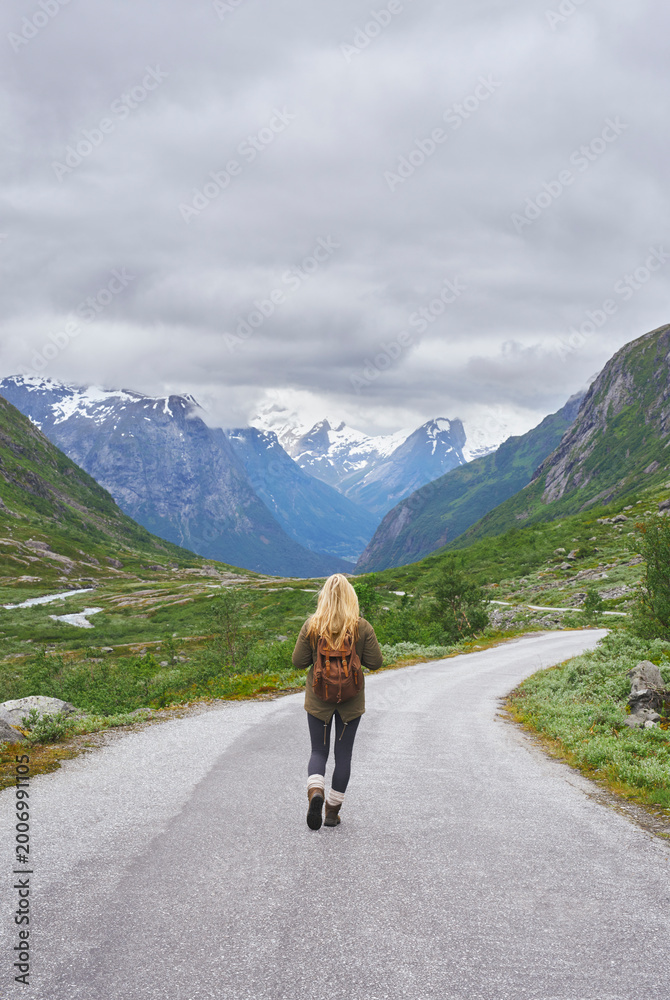 Fototapeta premium Mountain, backpacking and woman on road for adventure, mockup space and fresh air on journey or travel. Outdoor, person and hiking on weekend, exploration and trekking with view of valley and scenery