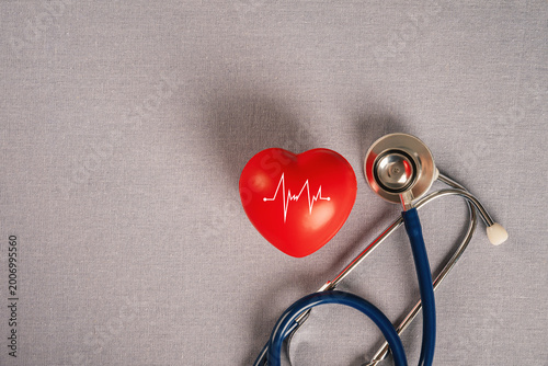 Red heart with an ECG pulse line and blue stethoscope on gray fabric background. for healthcare, cardiology, medical checkup, and heart disease awareness concepts.