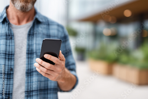 Close up of man holding smartphone in city background. Mobile technology for digital communication, social media app, and wireless internet connection in modern lifestyle.