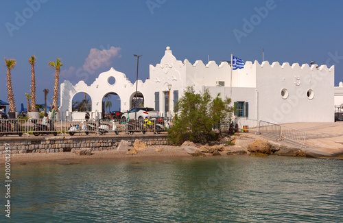 White harbor building with arches and Greek flag on waterfront in Rhodes Greece
