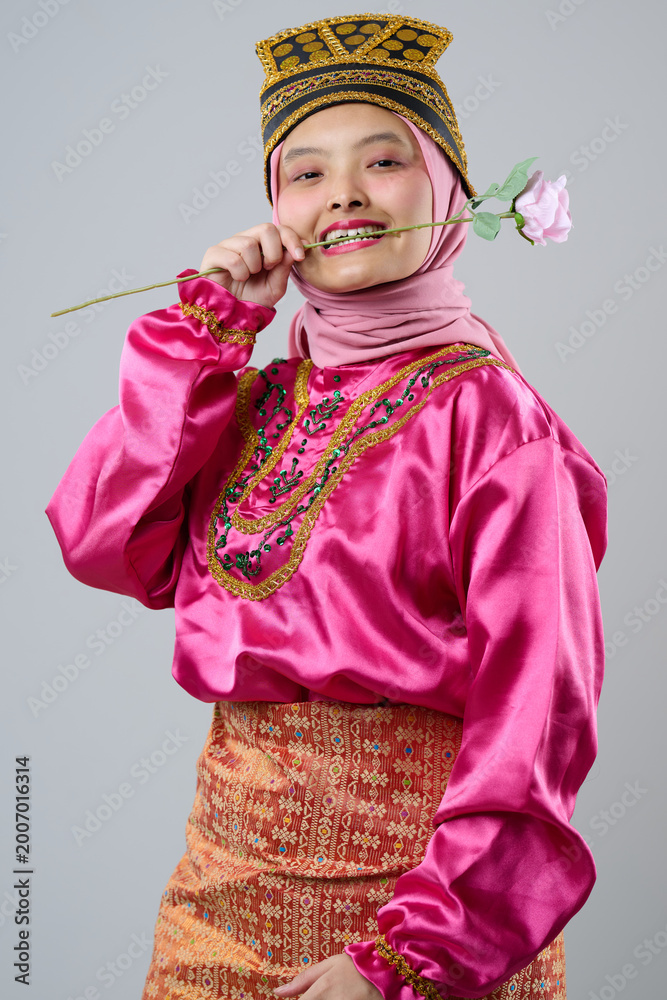 Obraz premium Young Indonesian Asian Woman In Pink Traditional Costume With Hijab And Decorative Headpiece Holding A Rose And Smiling