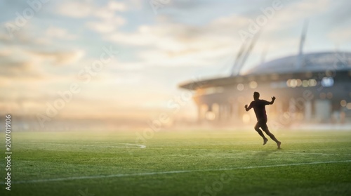Silhouette of a young male soccer player running on a professional stadium field at sunset