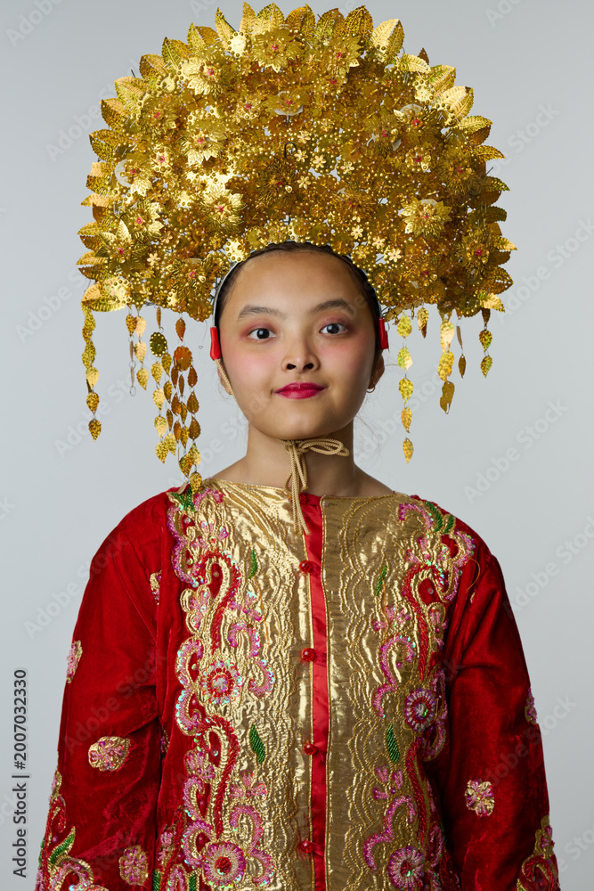 Fototapeta premium Young Indonesian Asian Girl Wearing Ornate Gold Headdress and Embroidered Red Traditional Costume Portrait