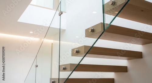A modern staircase with wooden steps and glass railing leads up to a bright skylight in a sleek interior
